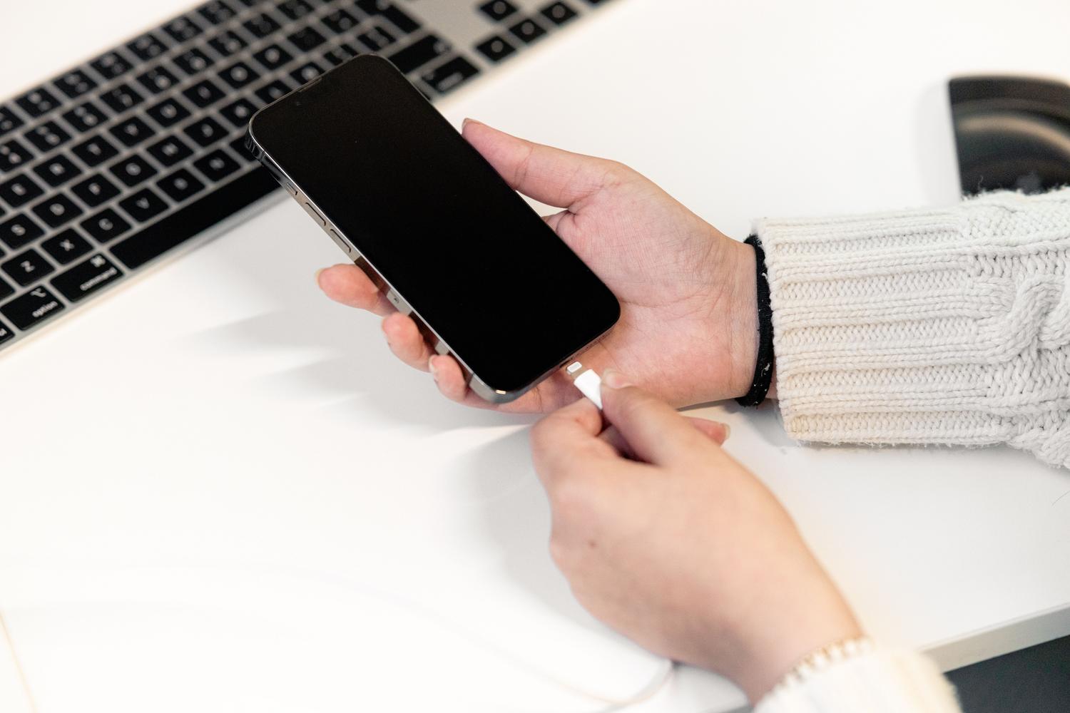 Close-up of a person connecting an iPhone to a computer using a USB cable.