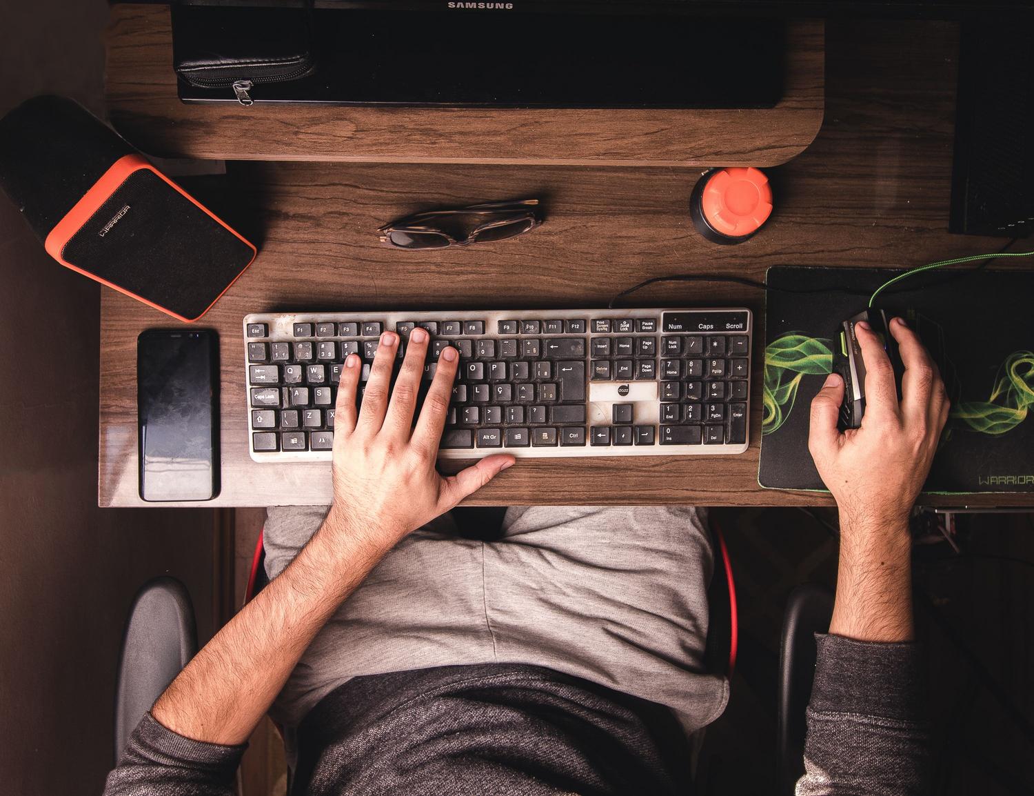 Hands using a keyboard and mouse on a desk.