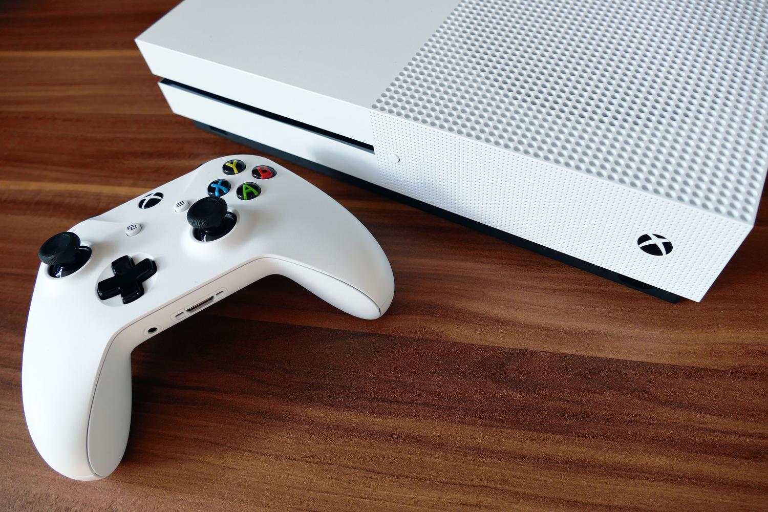 Consola Xbox One S y su mando blanco sobre una superficie de madera, proporcionando un toque lifestyle al contenido.