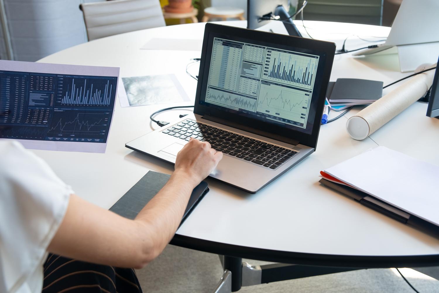 Professional evaluating financial tables and graphs on a laptop screen.