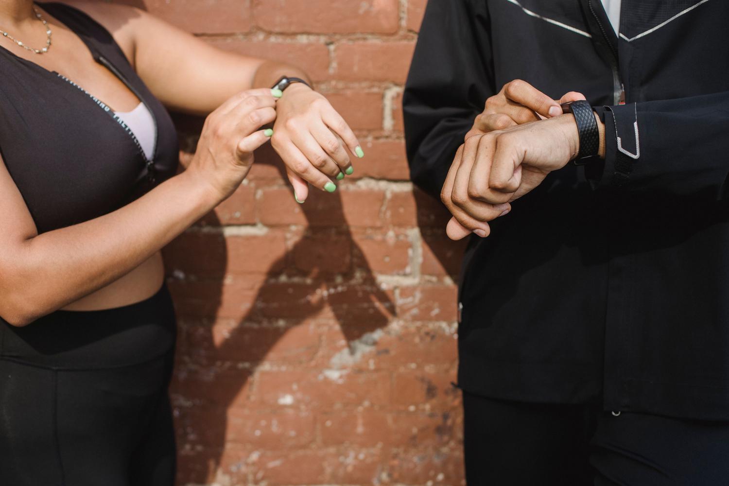 Dos personas con ropa deportiva revisando sus pulseras de actividad al aire libre.