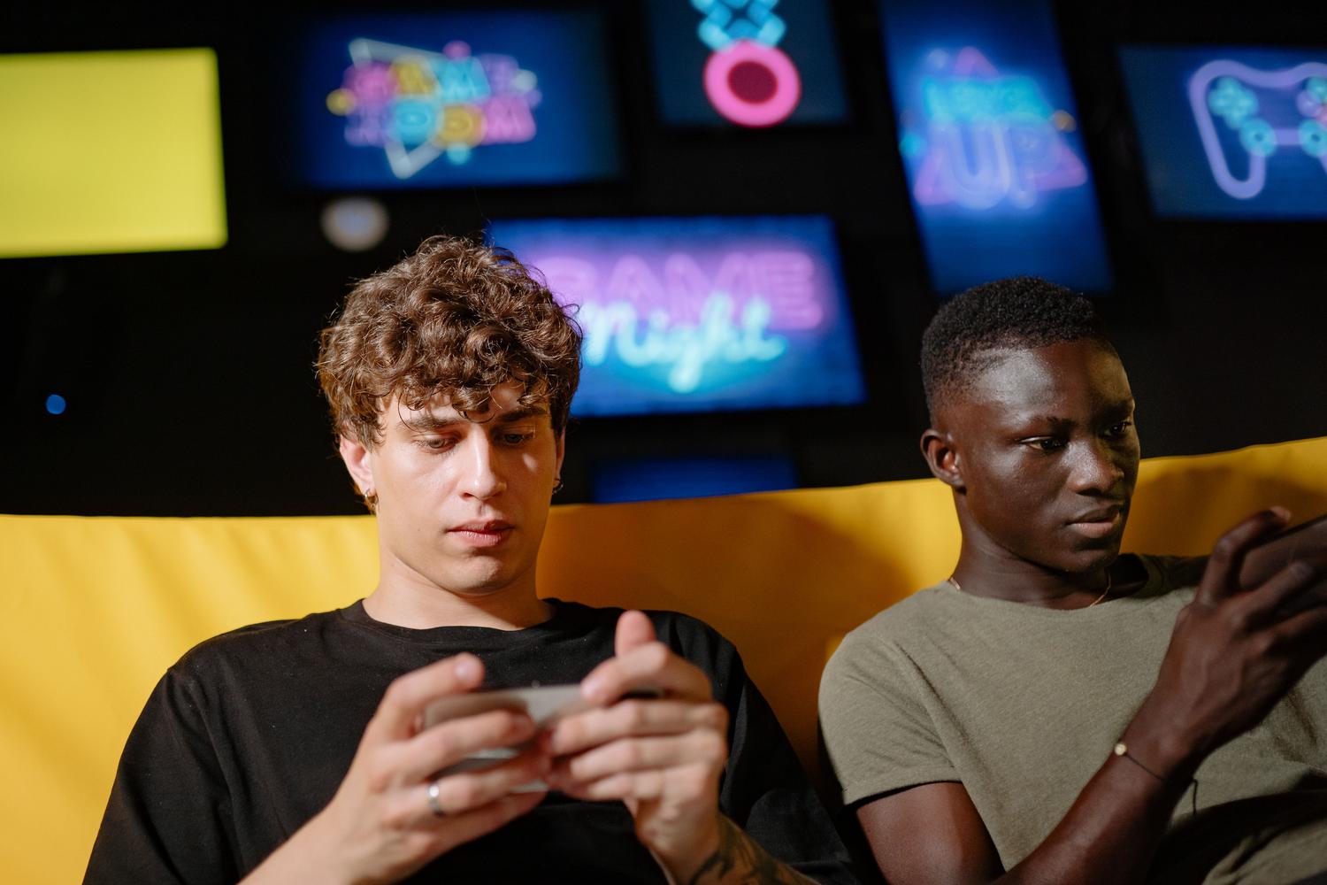 Dos amigos disfrutando juntos de una sesión de juegos en sus móviles, representando la comunidad y las funciones sociales de Game Finder.
