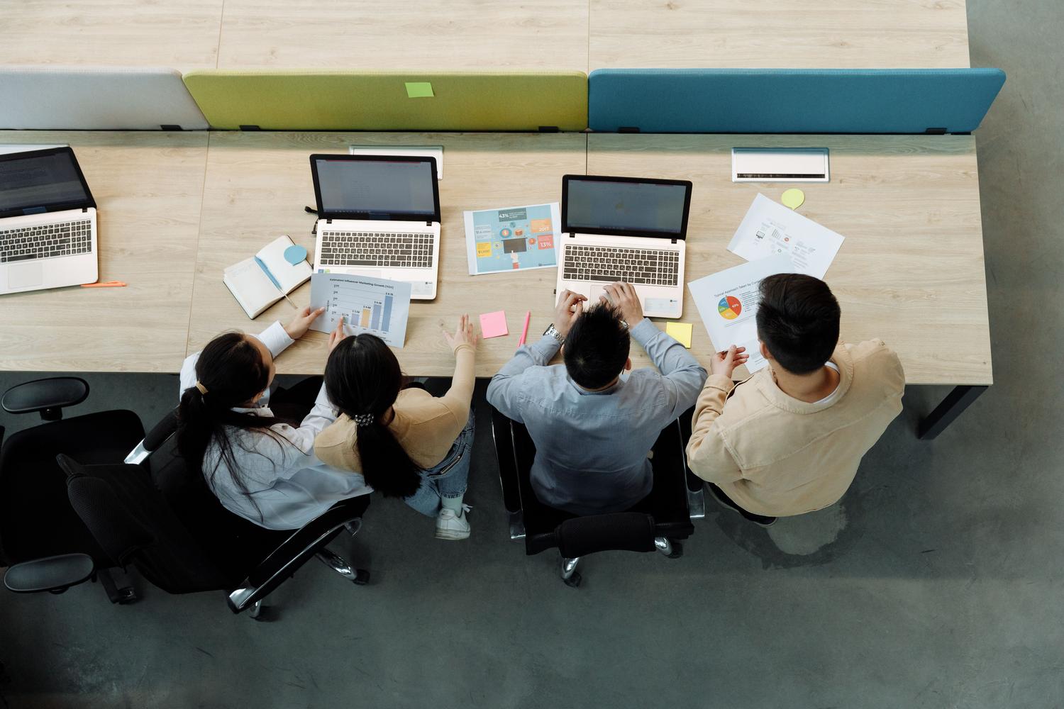 Vista cenital de personas trabajando con portátiles y documentos.