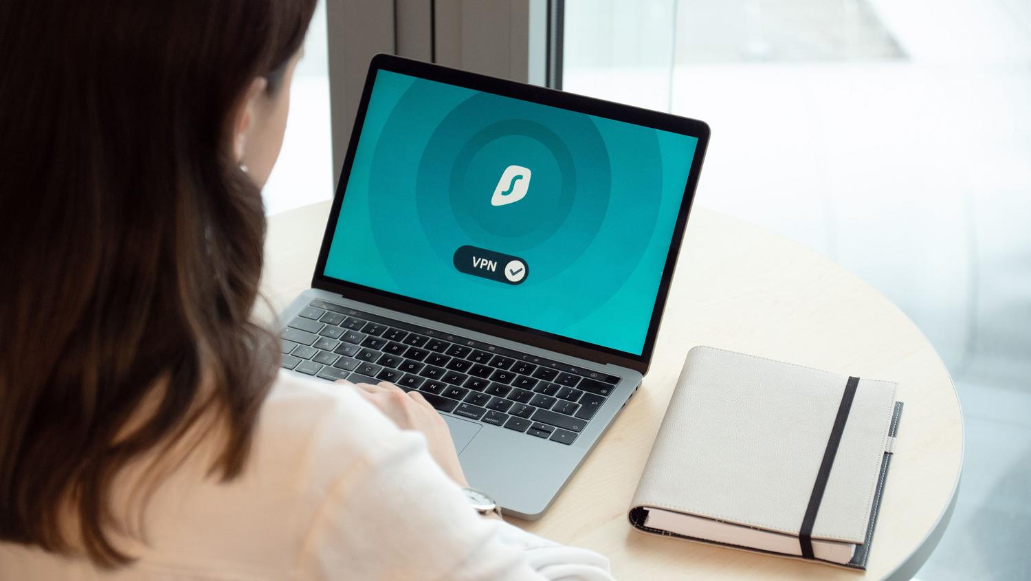Una persona trabajando en un portátil con un icono de VPN en pantalla, simbolizando el acceso remoto seguro y controlado.