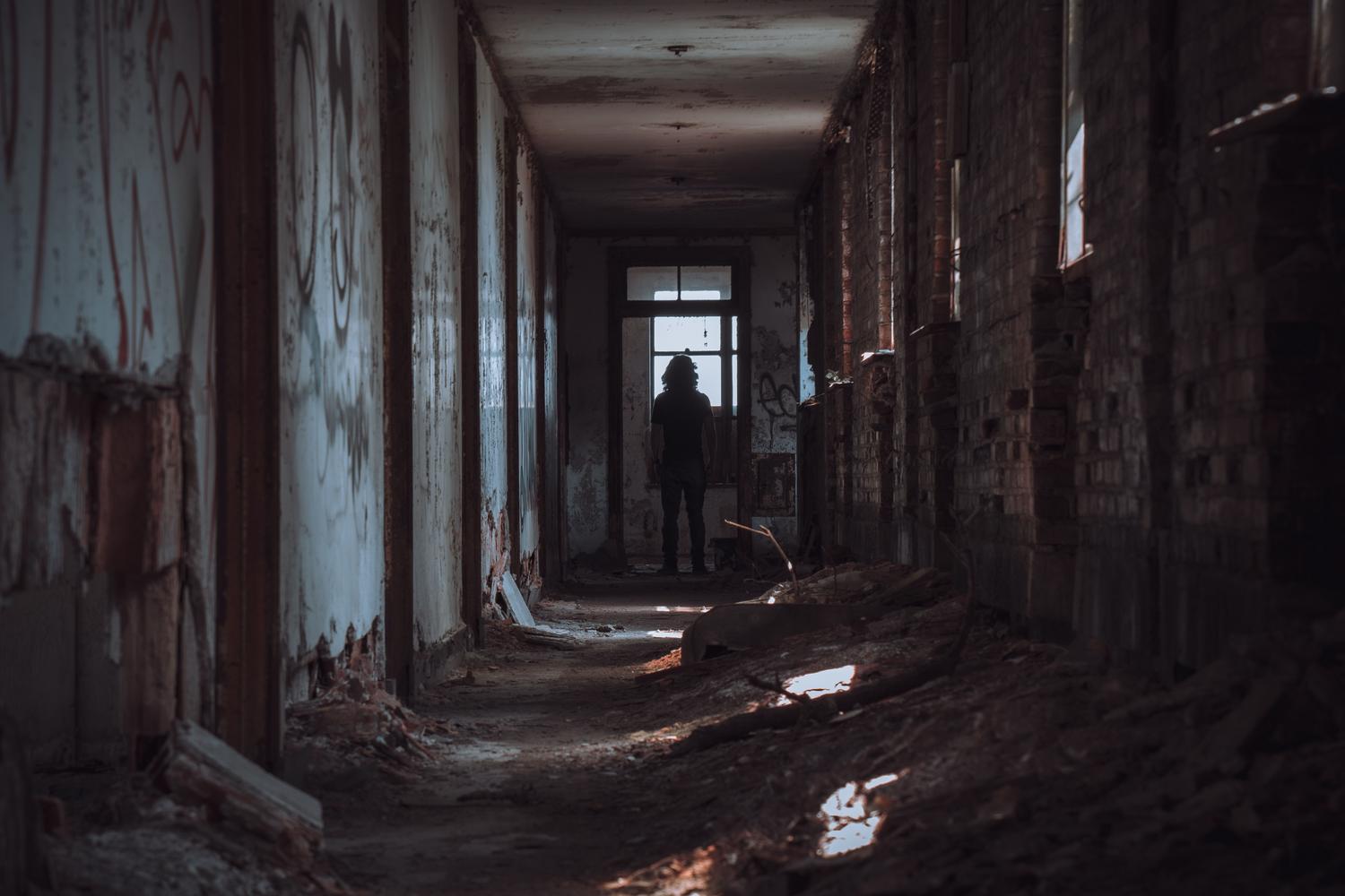 Figura solitaria en un pasillo abandonado y sombrío, ideal para representar la tensión de los juegos de investigación y misterio.