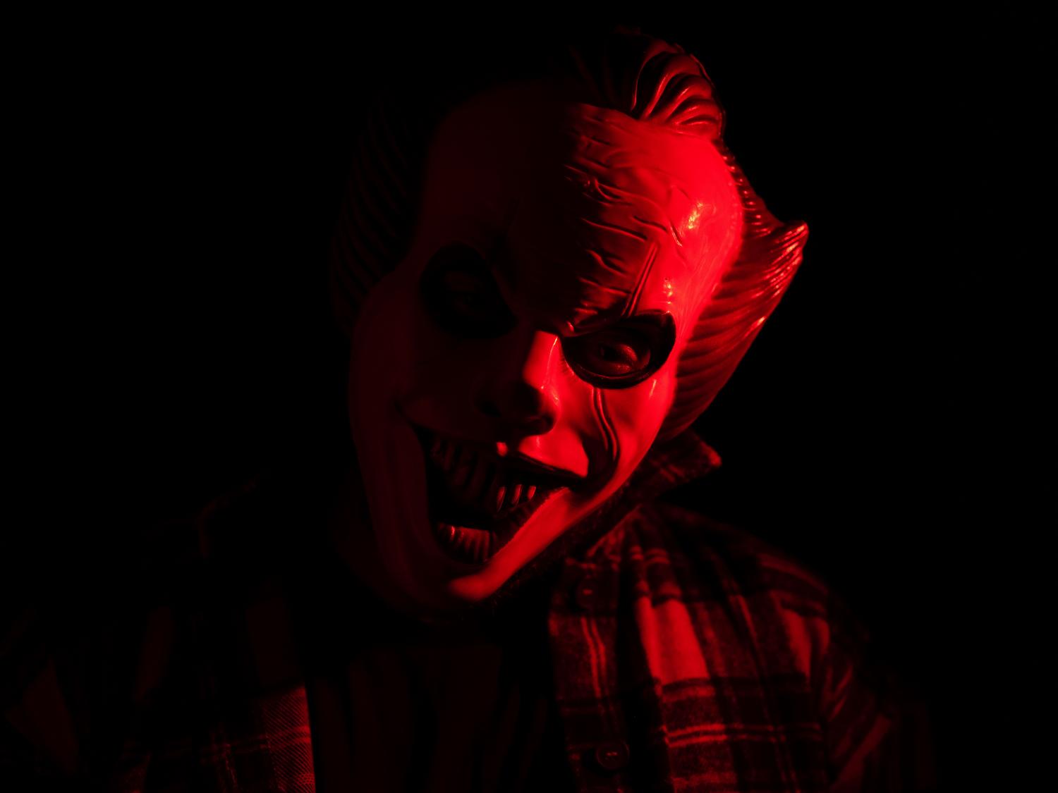 Figura enmascarada inquietante bajo una luz roja, simbolizando las entidades que acechan en la oscuridad.