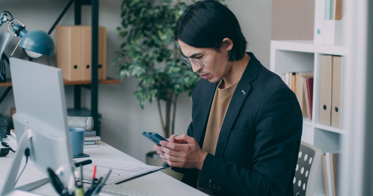 Joven profesional en una oficina utilizando su smartphone de manera eficiente.
