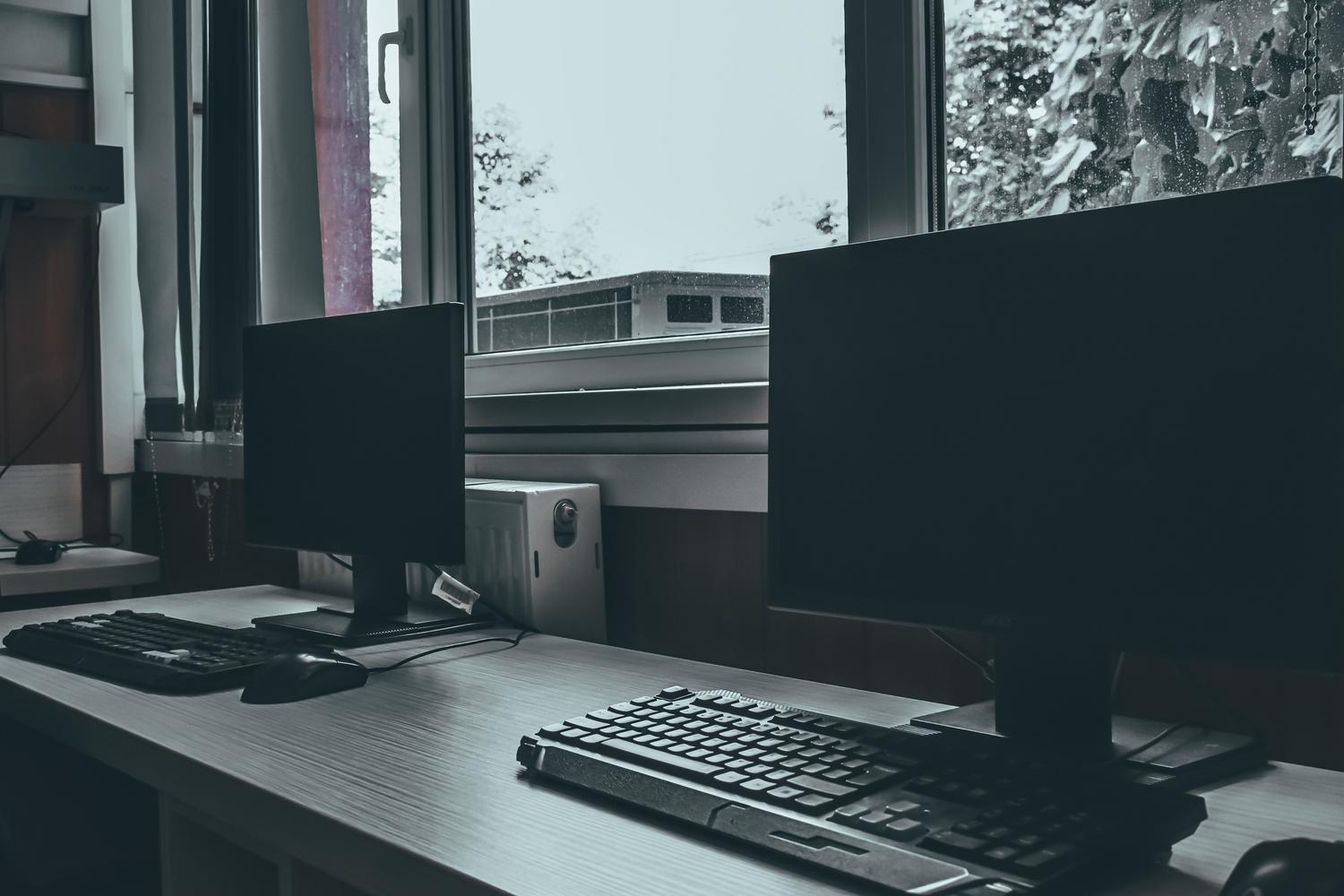 Dos monitores de ordenador con la pantalla totalmente negra sobre un escritorio moderno, representando el error de pantalla negra en Windows 11.