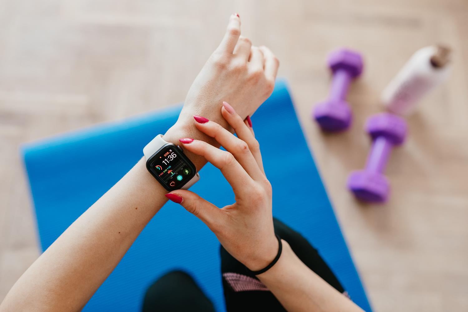 Mujer en ropa deportiva sobre una esterilla de yoga consultando su reloj inteligente para monitorizar su recuperación y bienestar.