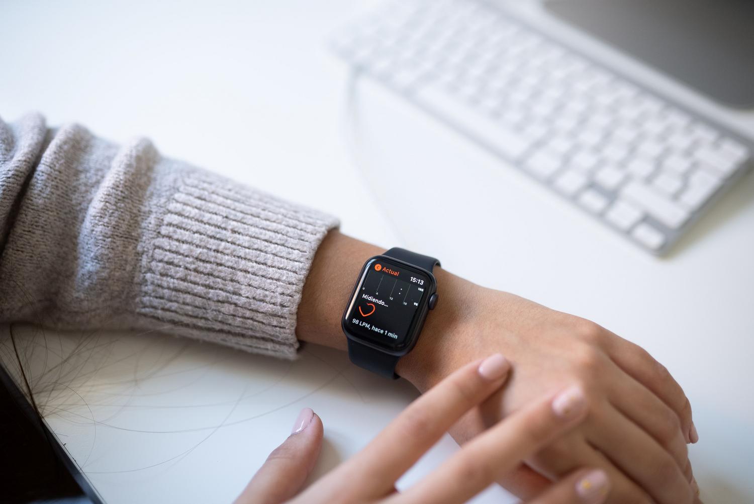 Persona revisando sus estadísticas de salud en un smartwatch mientras trabaja en una oficina, ilustrando la integración de la salud digital en la rutina diaria.