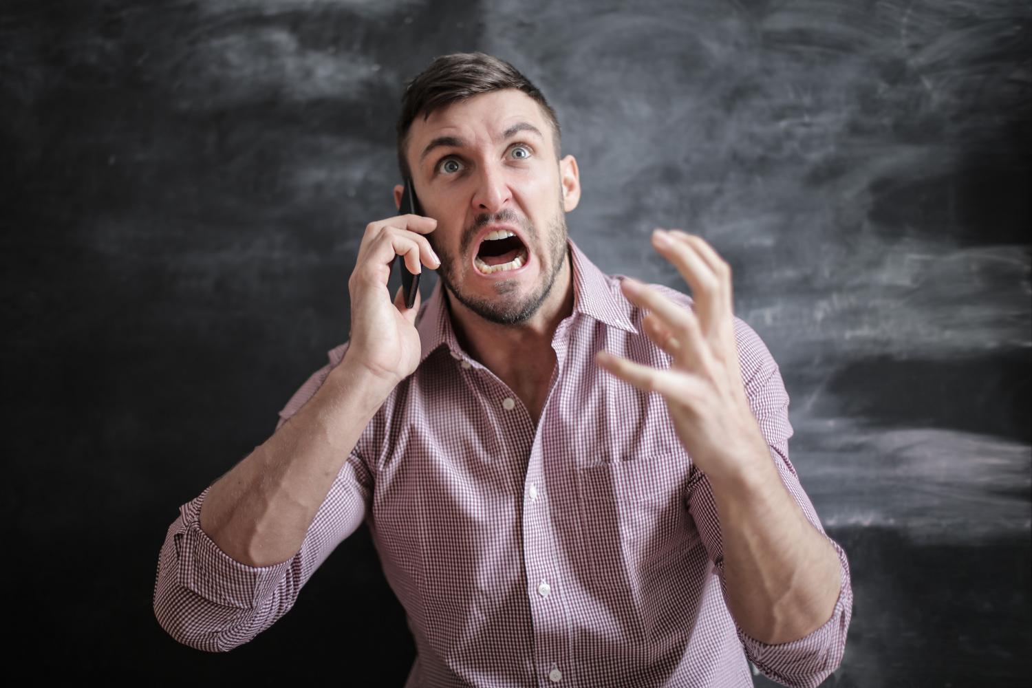 Hombre frustrado mientras utiliza su teléfono móvil, representando los errores y fallos del sistema operativo.