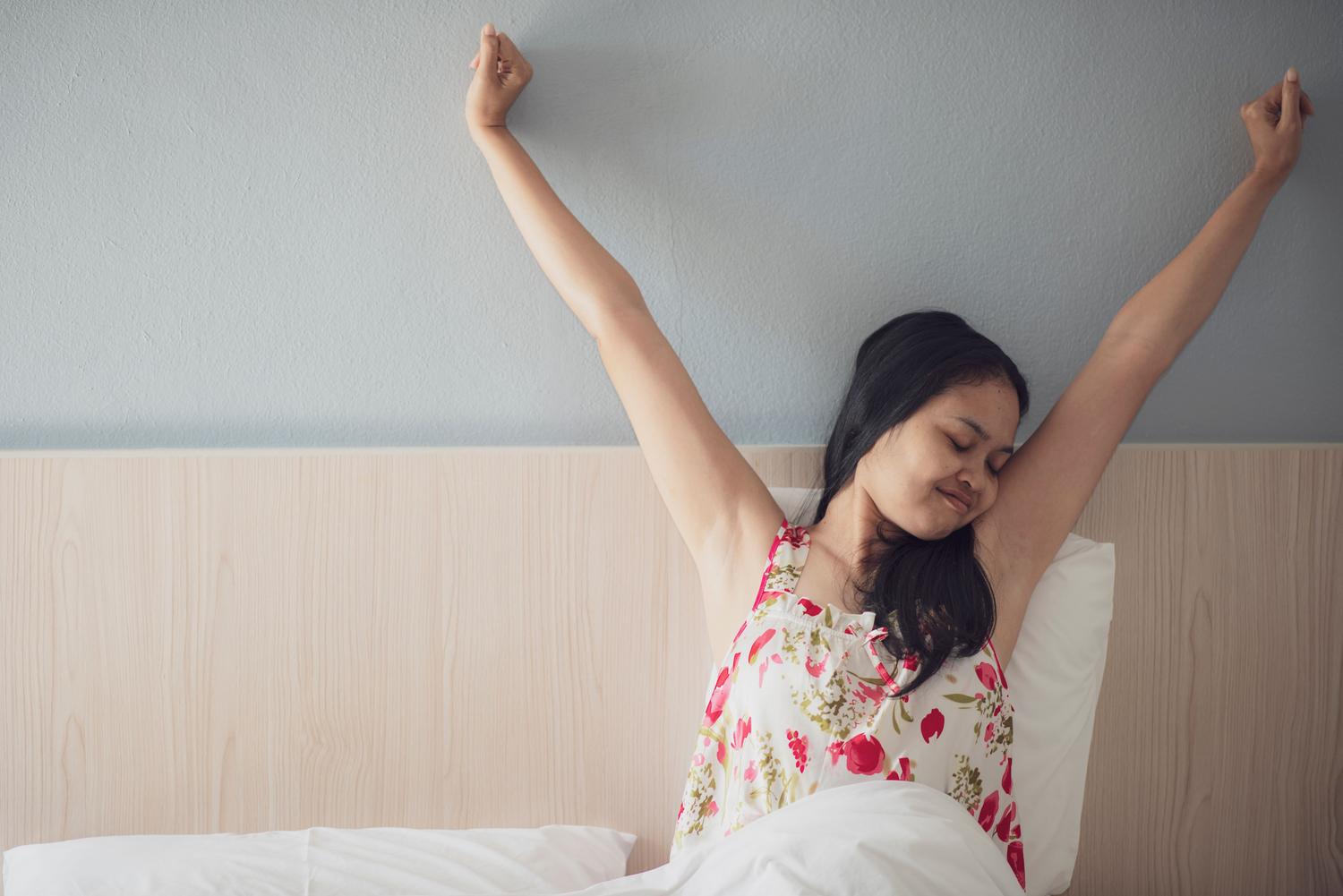 Una mujer estirándose al despertar en la cama con energía, reflejando un Energy Score positivo y una buena satisfacción del sueño.