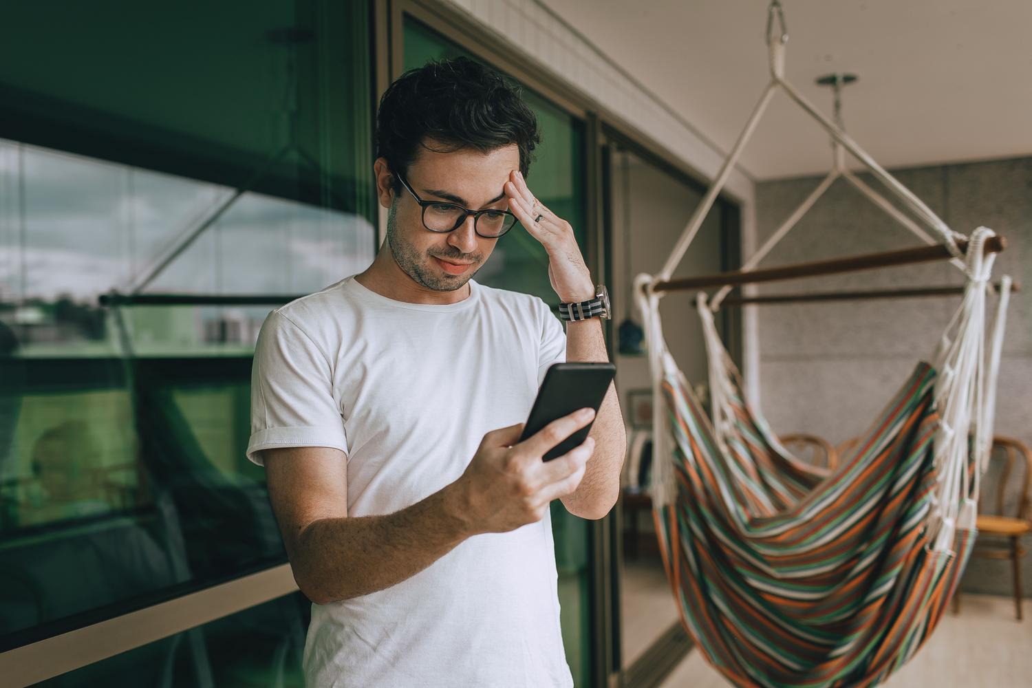 Een man kijkt met een gefrustreerde uitdrukking naar zijn mobiele telefoon.