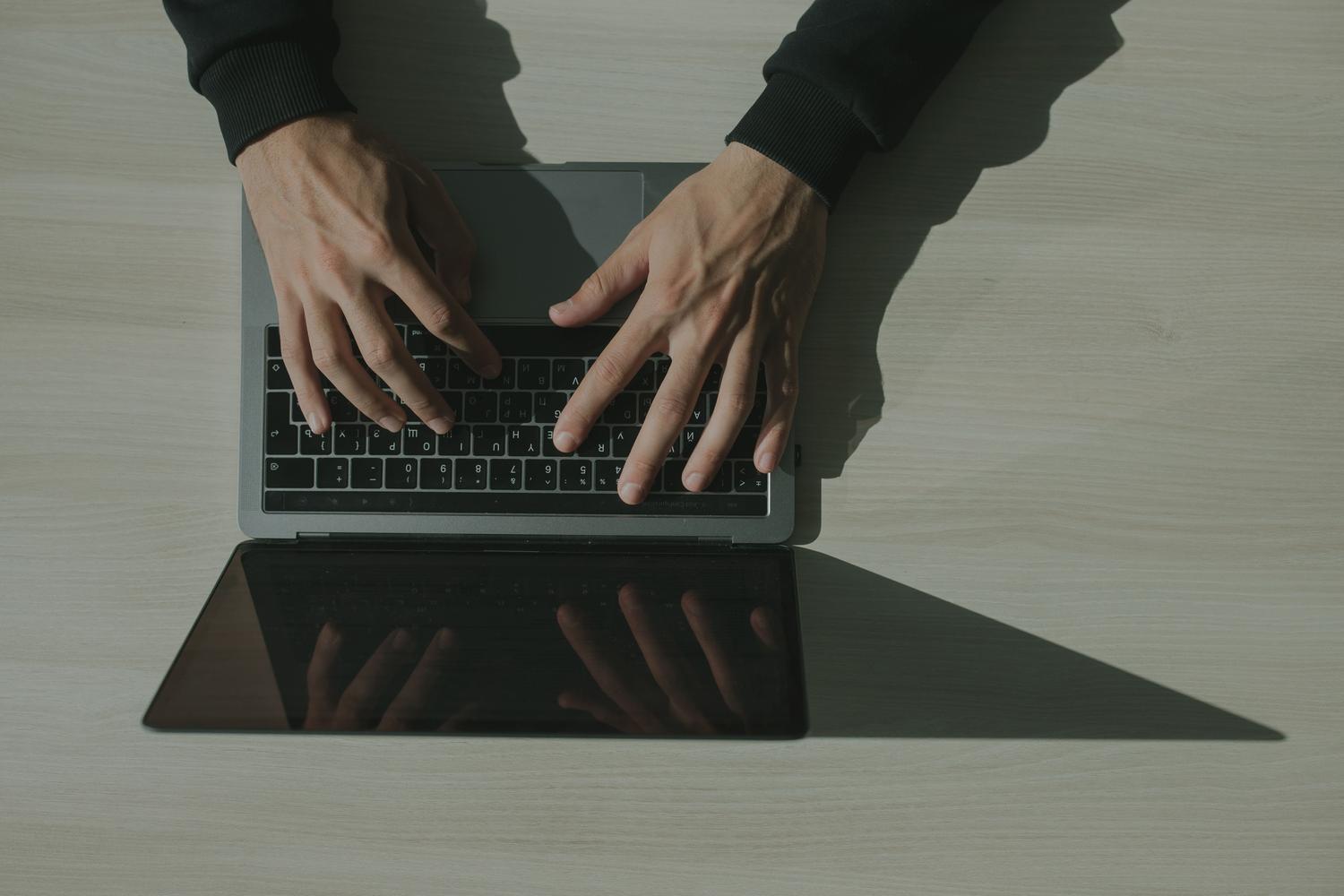 Manos escribiendo en el teclado de un ordenador portátil.
