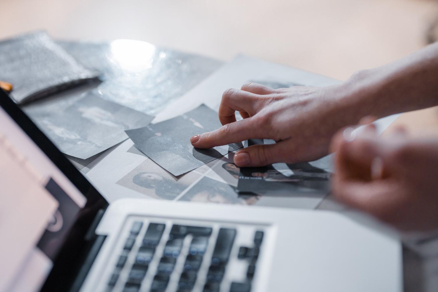 Hand arranging old photographs next to a computer, symbolizing the recovery of digital memories
