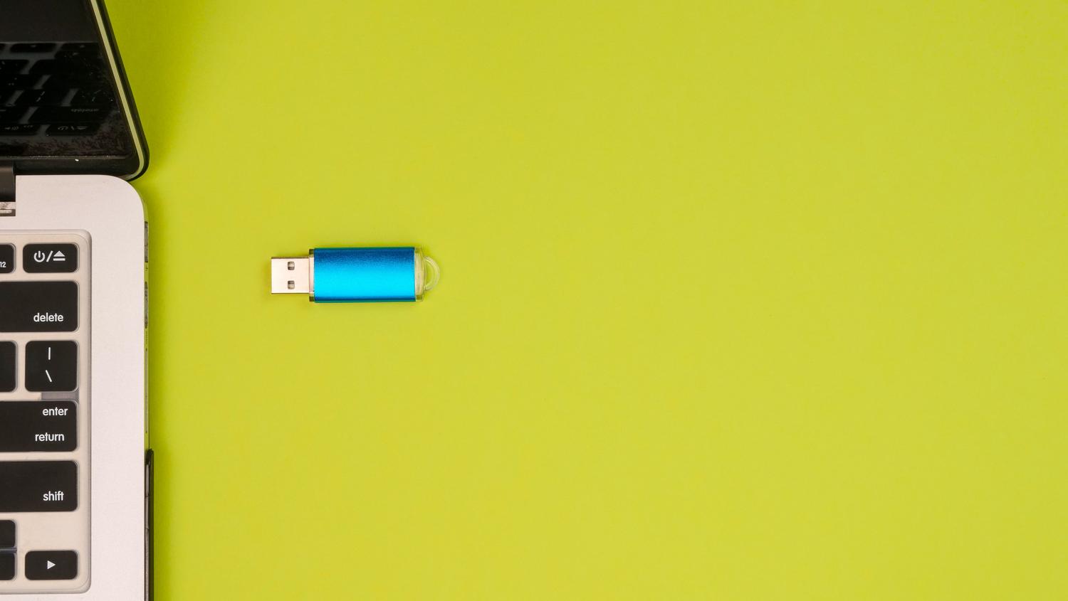 Memoria USB azul junto a un portátil sobre un fondo amarillo vibrante