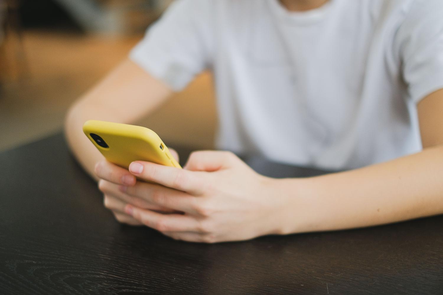 Primer plano de manos sosteniendo un smartphone con funda amarilla, interactuando con la pantalla.