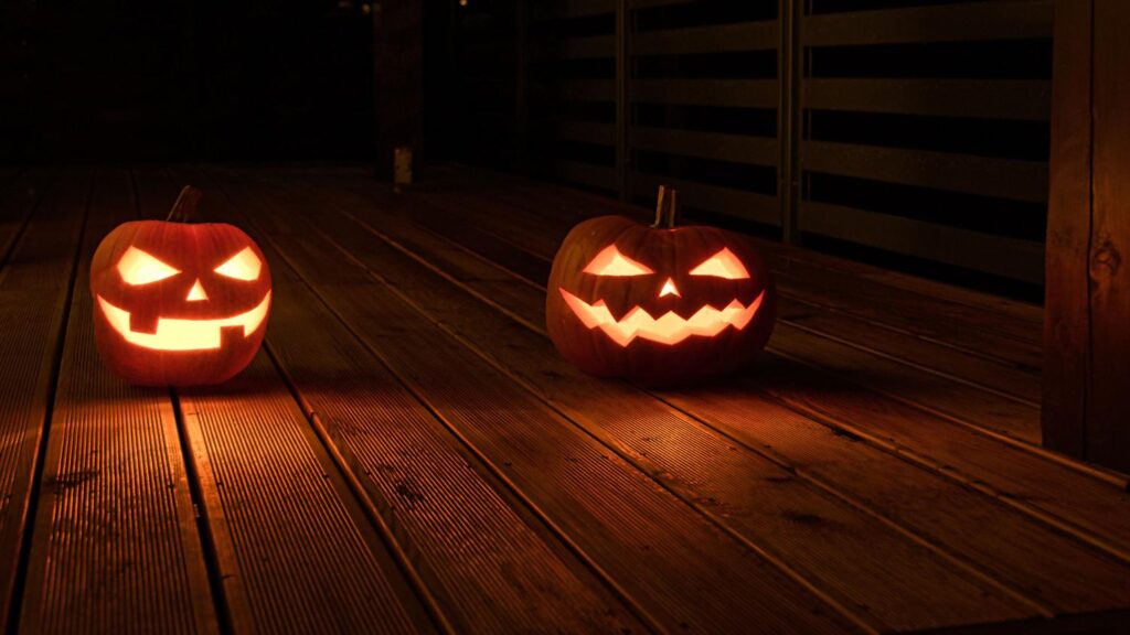 Dos calabazas de Halloween iluminadas sobre un porche de madera oscura, creando una atmósfera misteriosa y cinematográfica