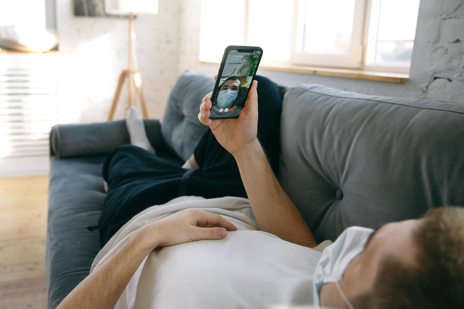 Hombre realizando una videollamada desde su smartphone en el sofá de su casa, ilustrando el uso cotidiano de las comunicaciones virtuales.