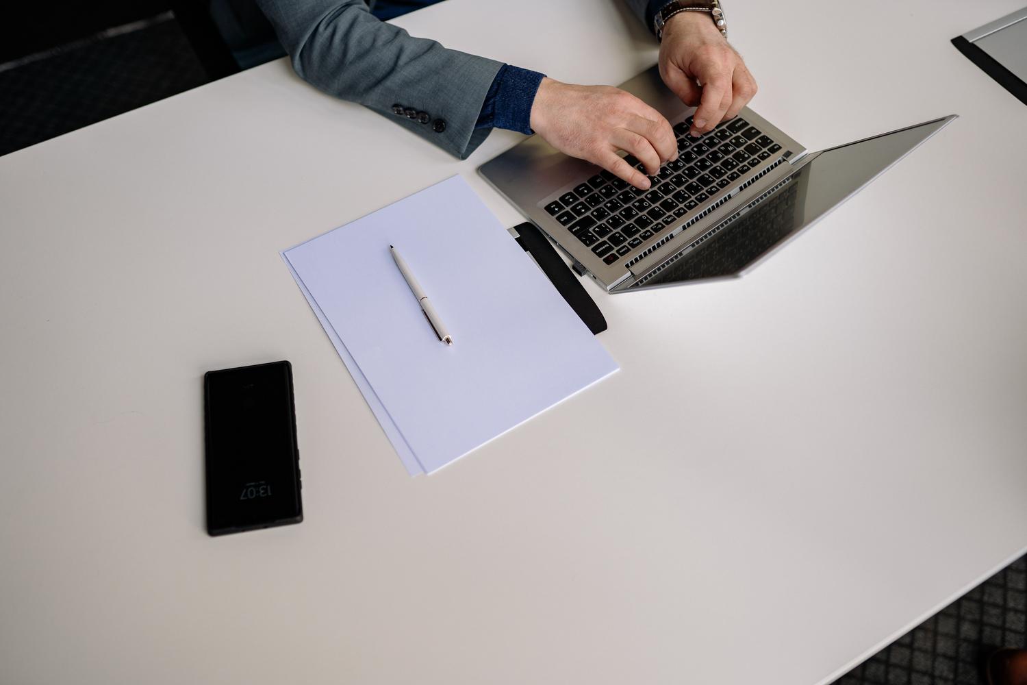 Vista cenital de una persona escribiendo en un portátil sobre un escritorio blanco.