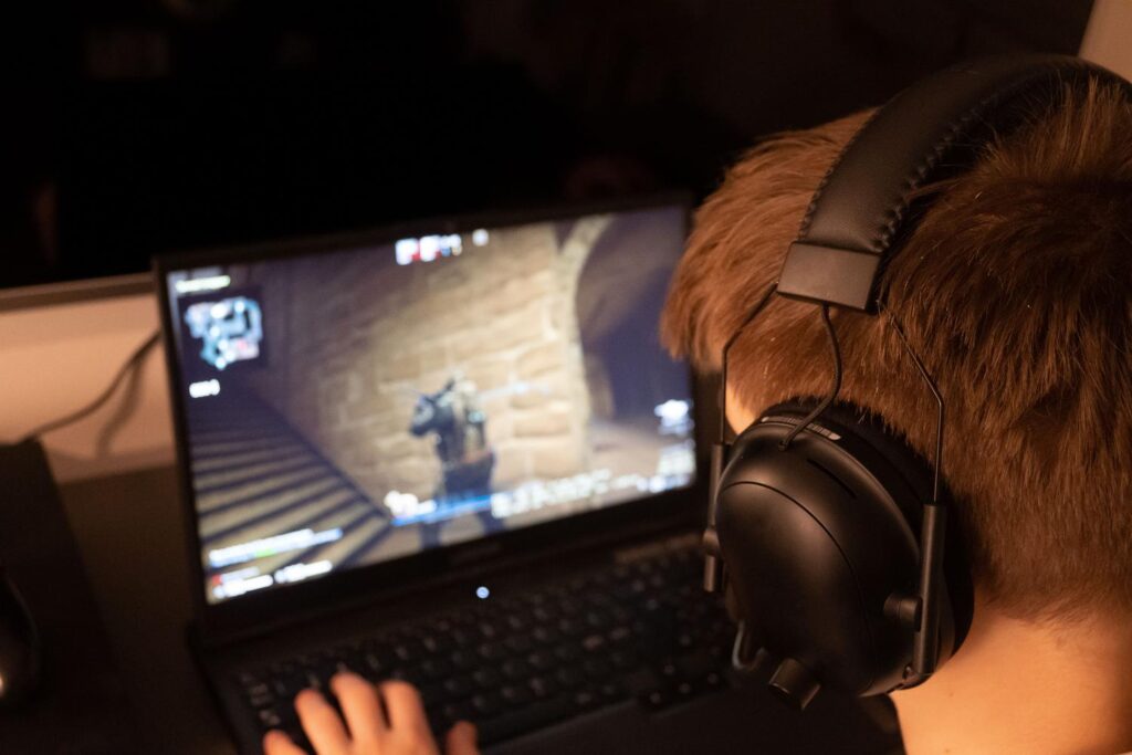 Persona concentrada jugando a un videojuego en un ordenador portátil con auriculares, representando la experiencia de gaming en la nube.