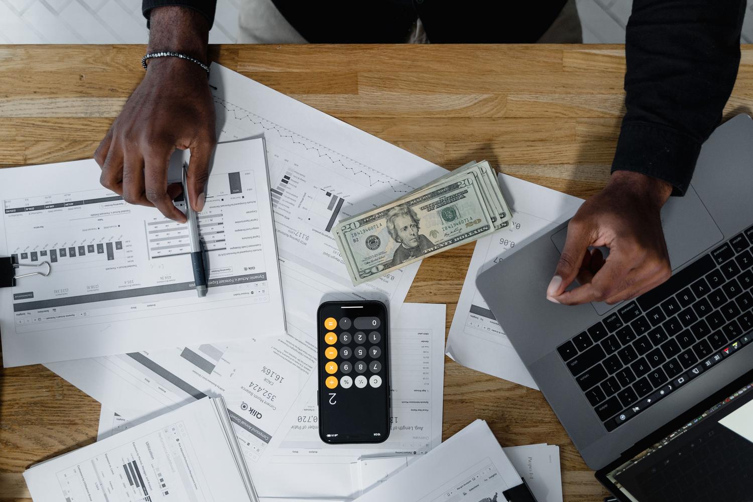 Manos trabajando con datos junto a un portátil y una calculadora.